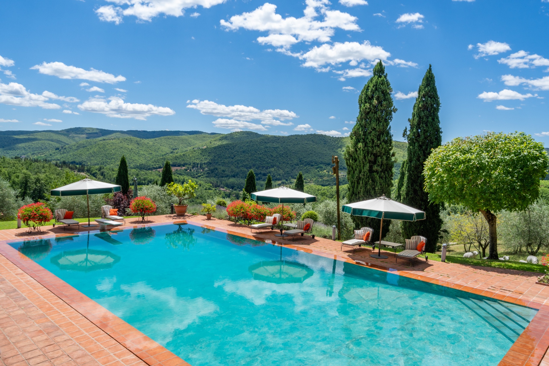 Elevated wide view of the infinity pool framed by cypress and umbrellas, looking out over the Chianti hills