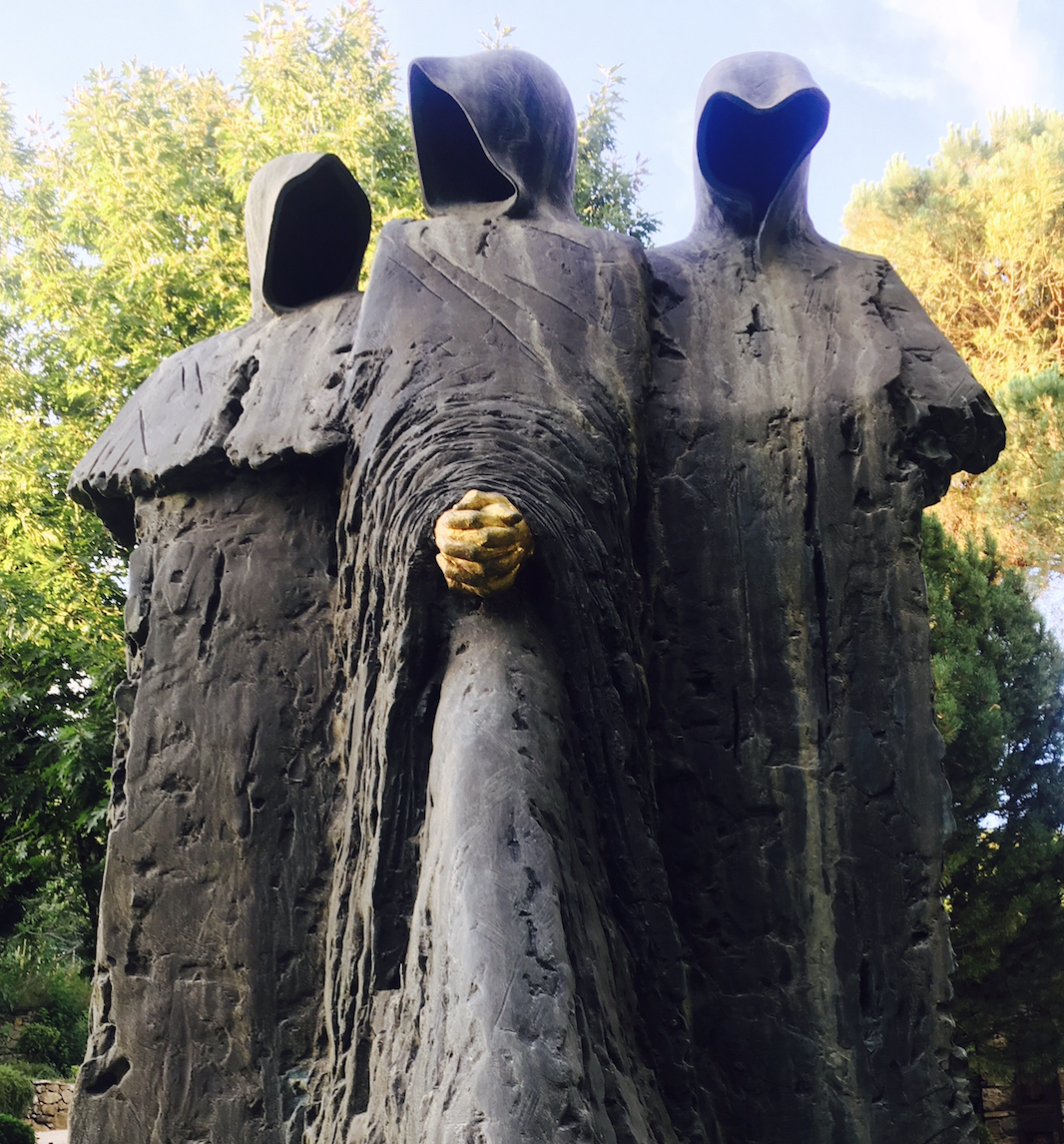 Bronze sculpture of three hooded cloaked figures standing close together in the garden
