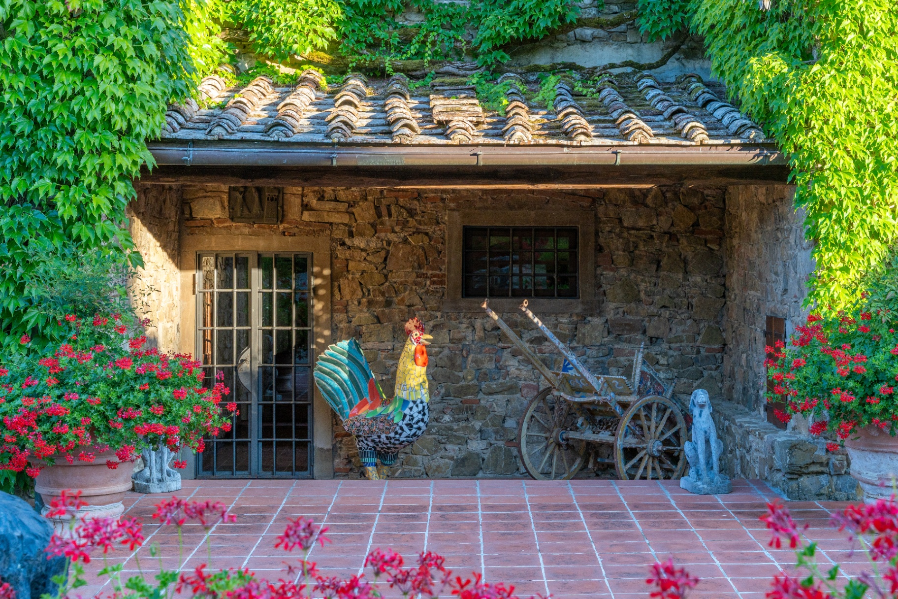 Mosaic rooster, antique cart and geraniums at the ivy-clad estate cottage
