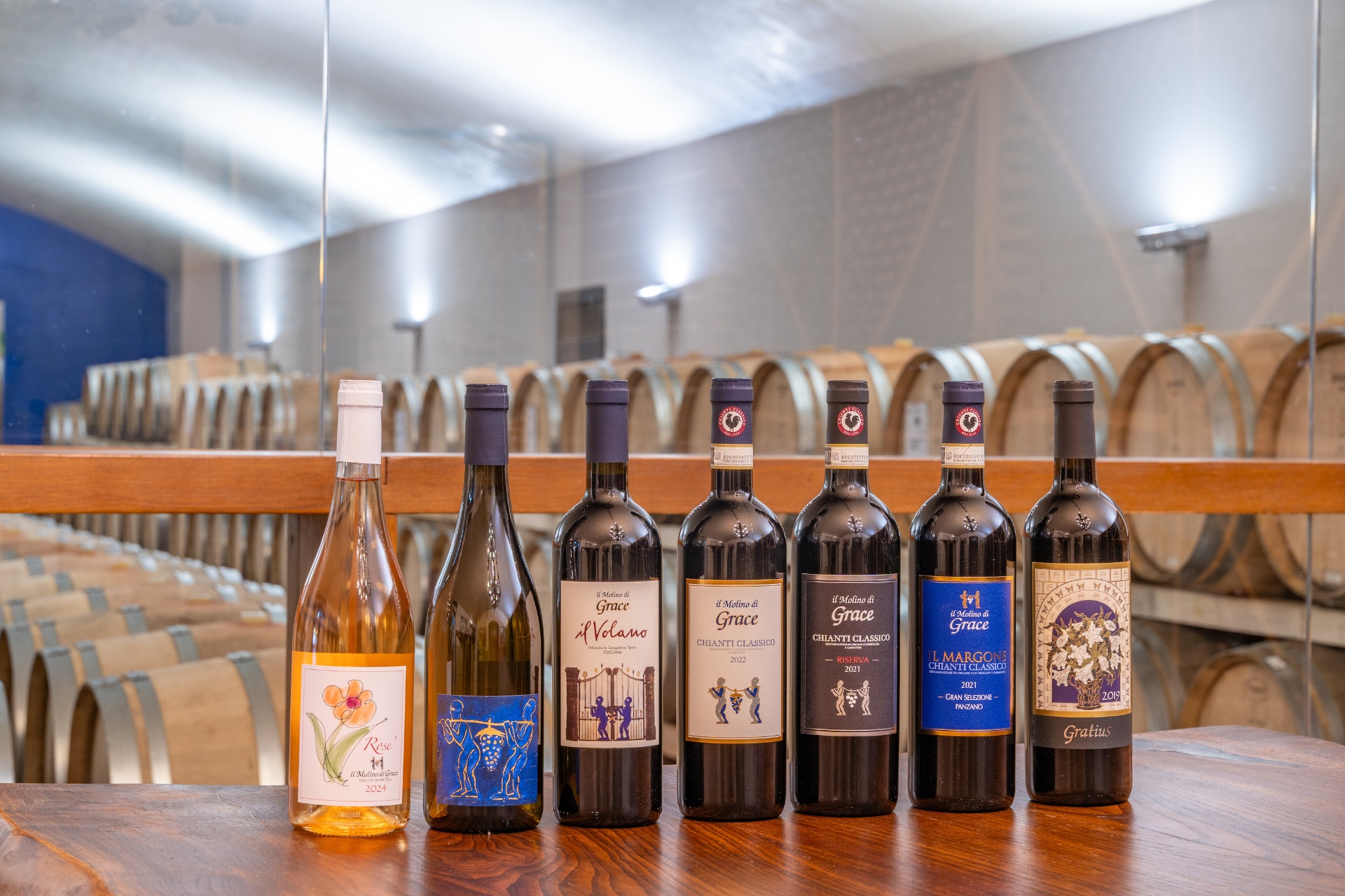 Seven Il Molino di Grace wine bottles lined up on a wooden surface in the barrel cellar
