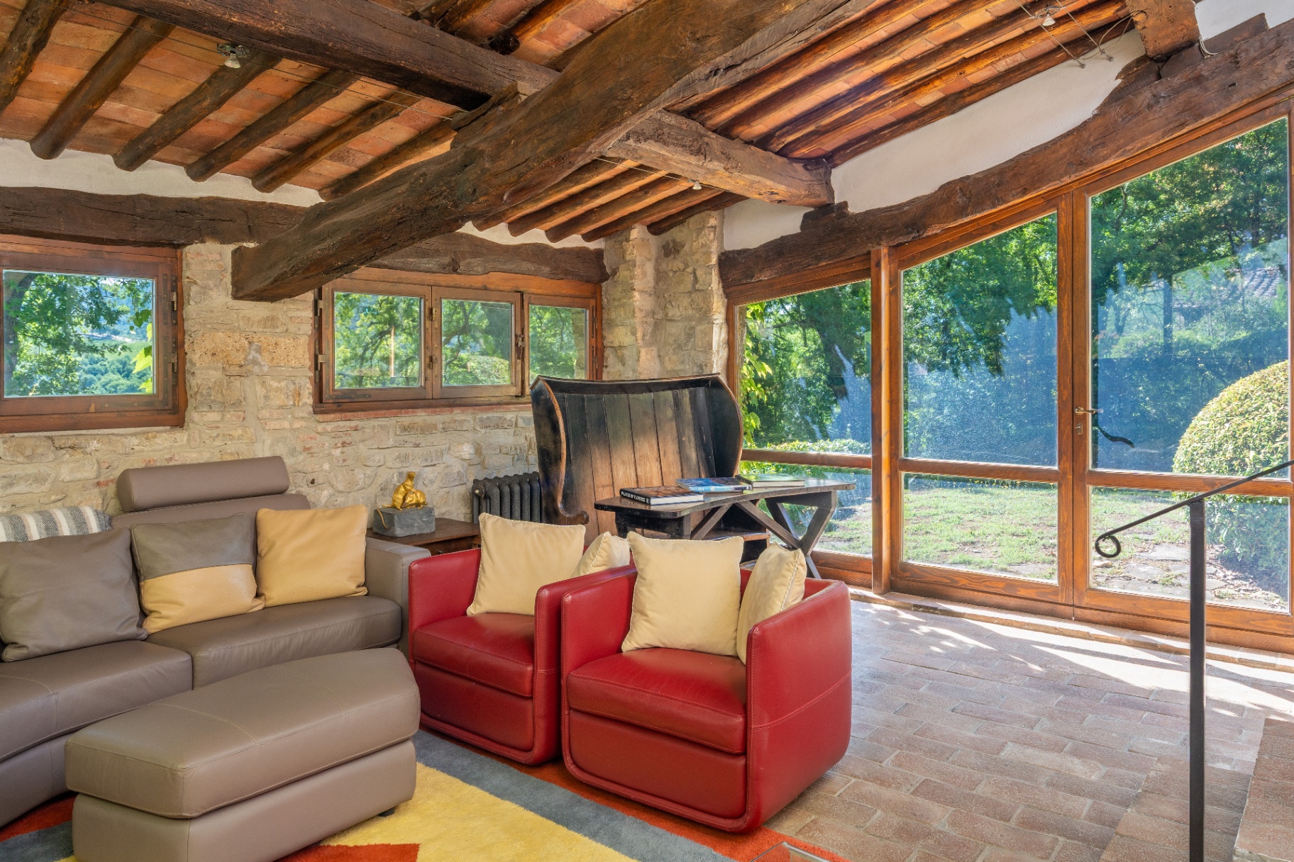 Sun-filled living room with timber beams, stone walls and wide windows onto the garden
