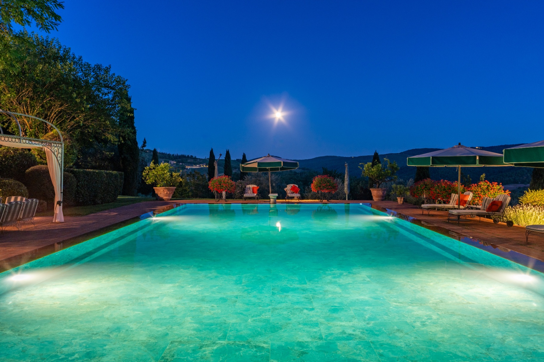 The infinity pool glowing at twilight under a full moon with the Chianti hills beyond