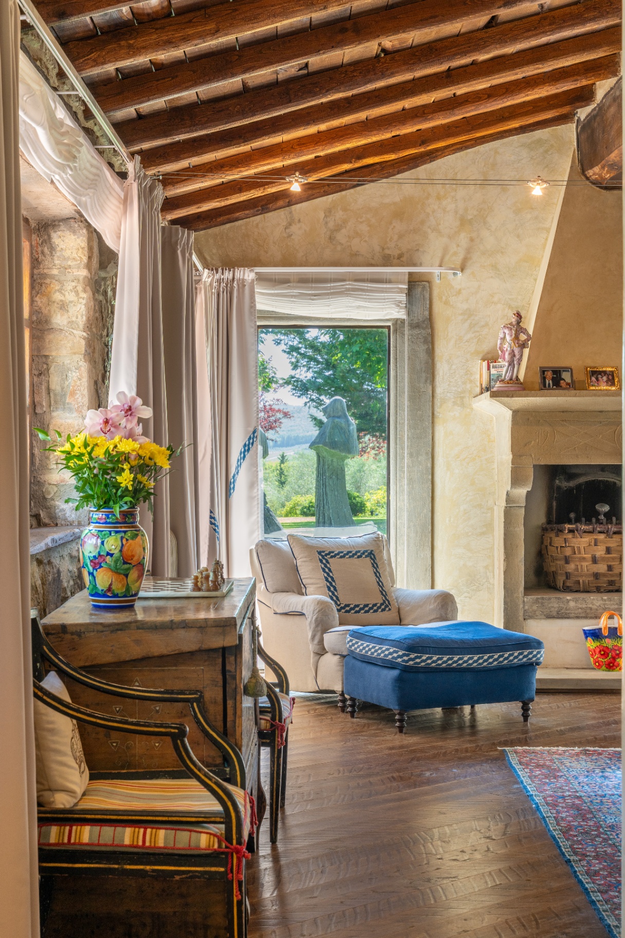Rustic sitting room with beamed ceiling, fireplace and a view to a garden sculpture