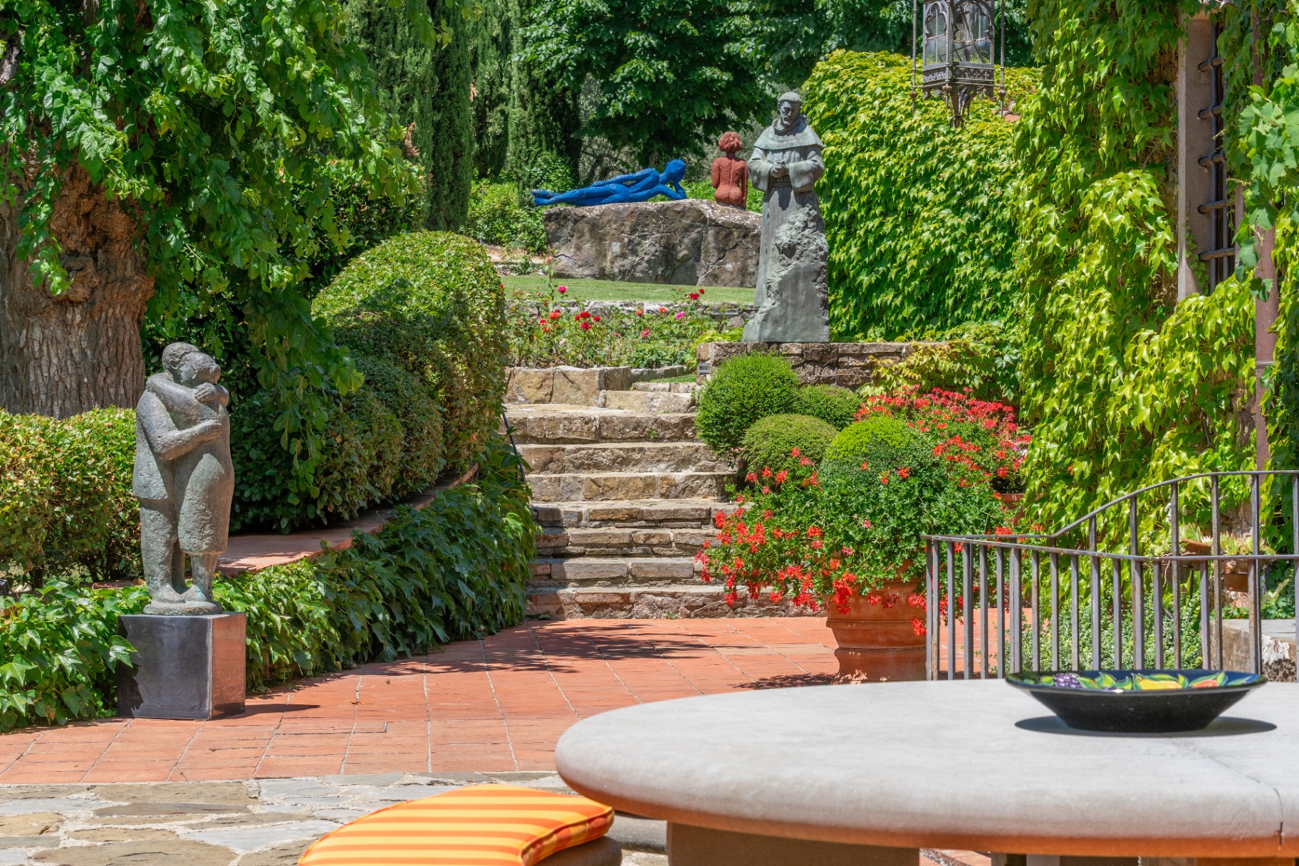 Stone garden steps framed by sculptures, topiary and flowering geraniums