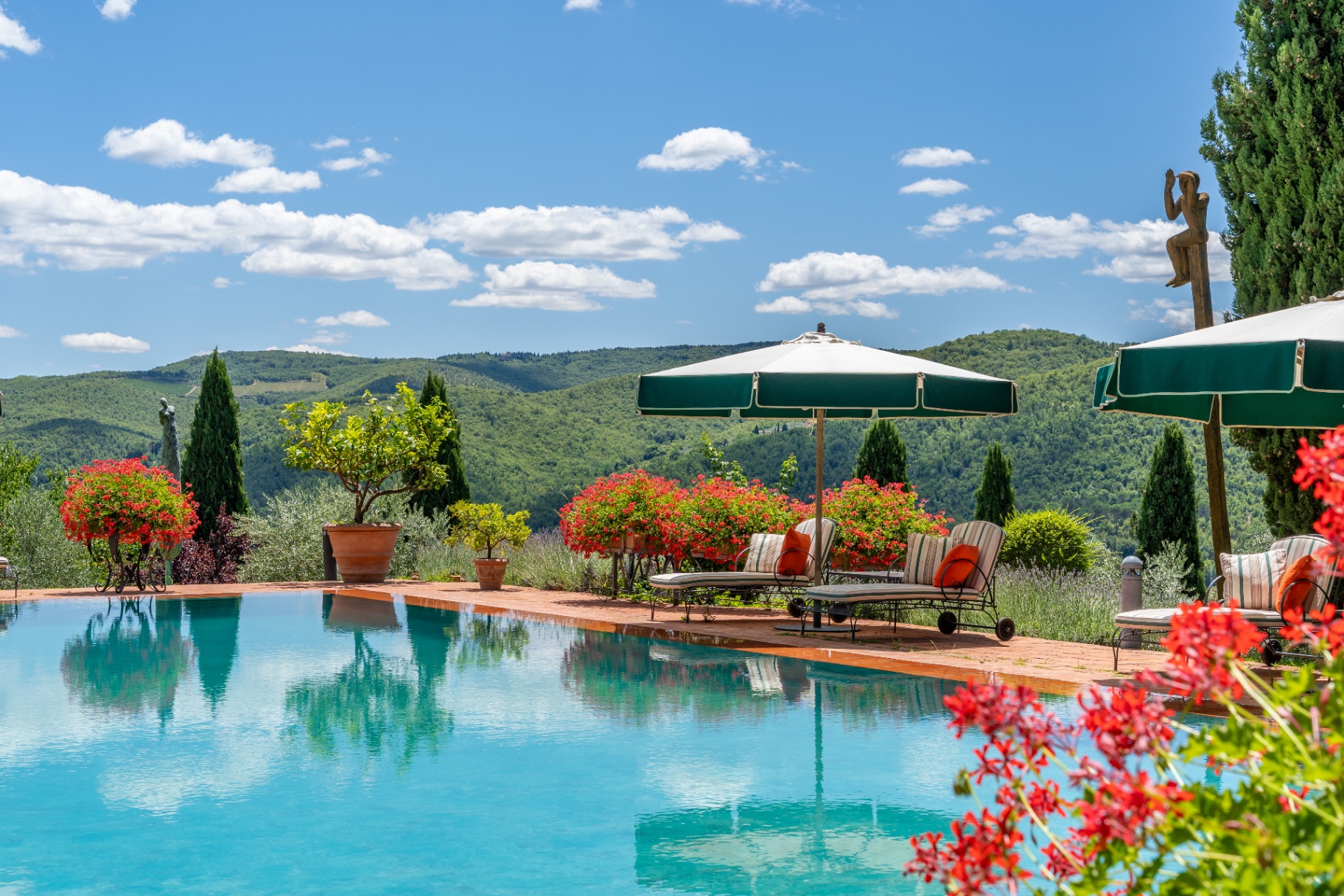 Infinity pool with green umbrellas, lounge chairs and red geraniums overlooking the Chianti hills