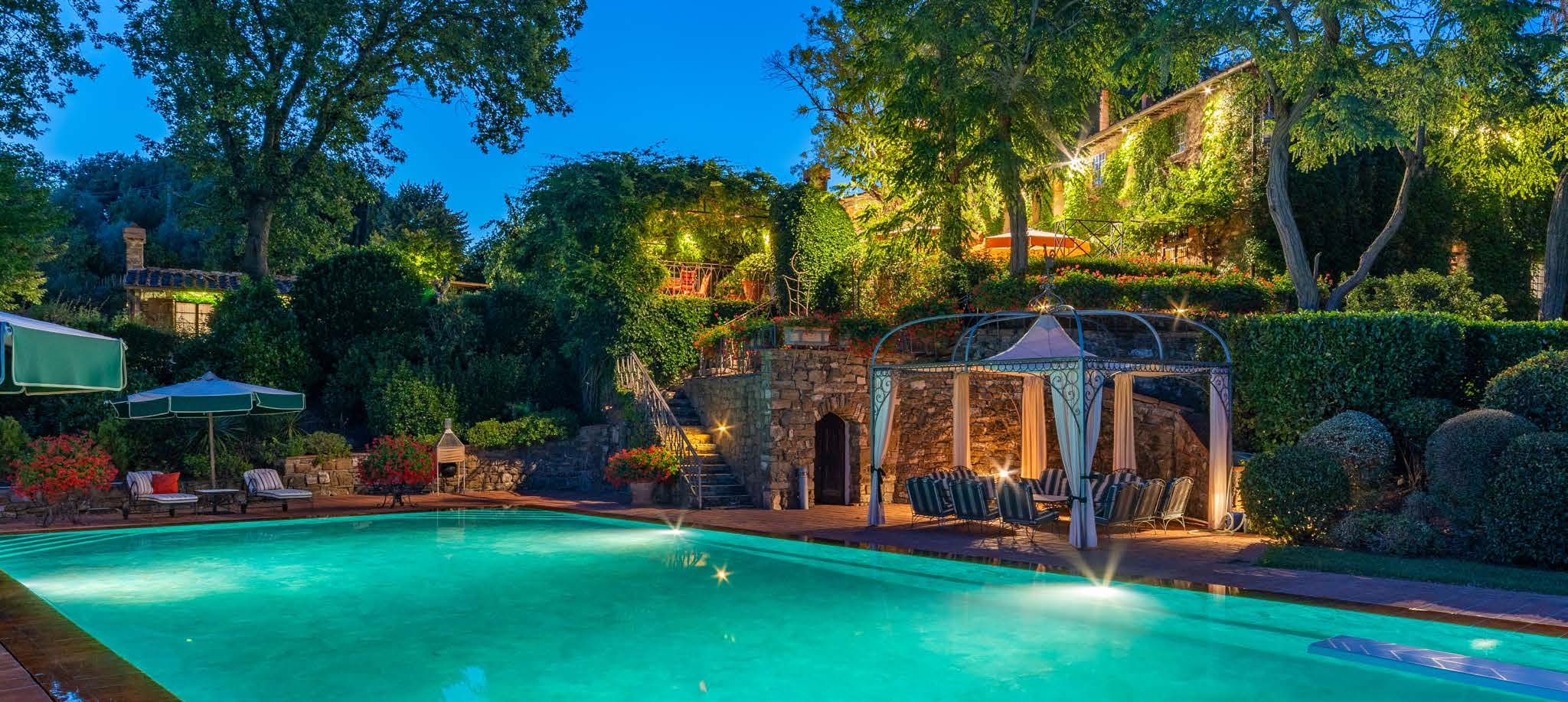 The pool at dusk with the stone house and lush greenery