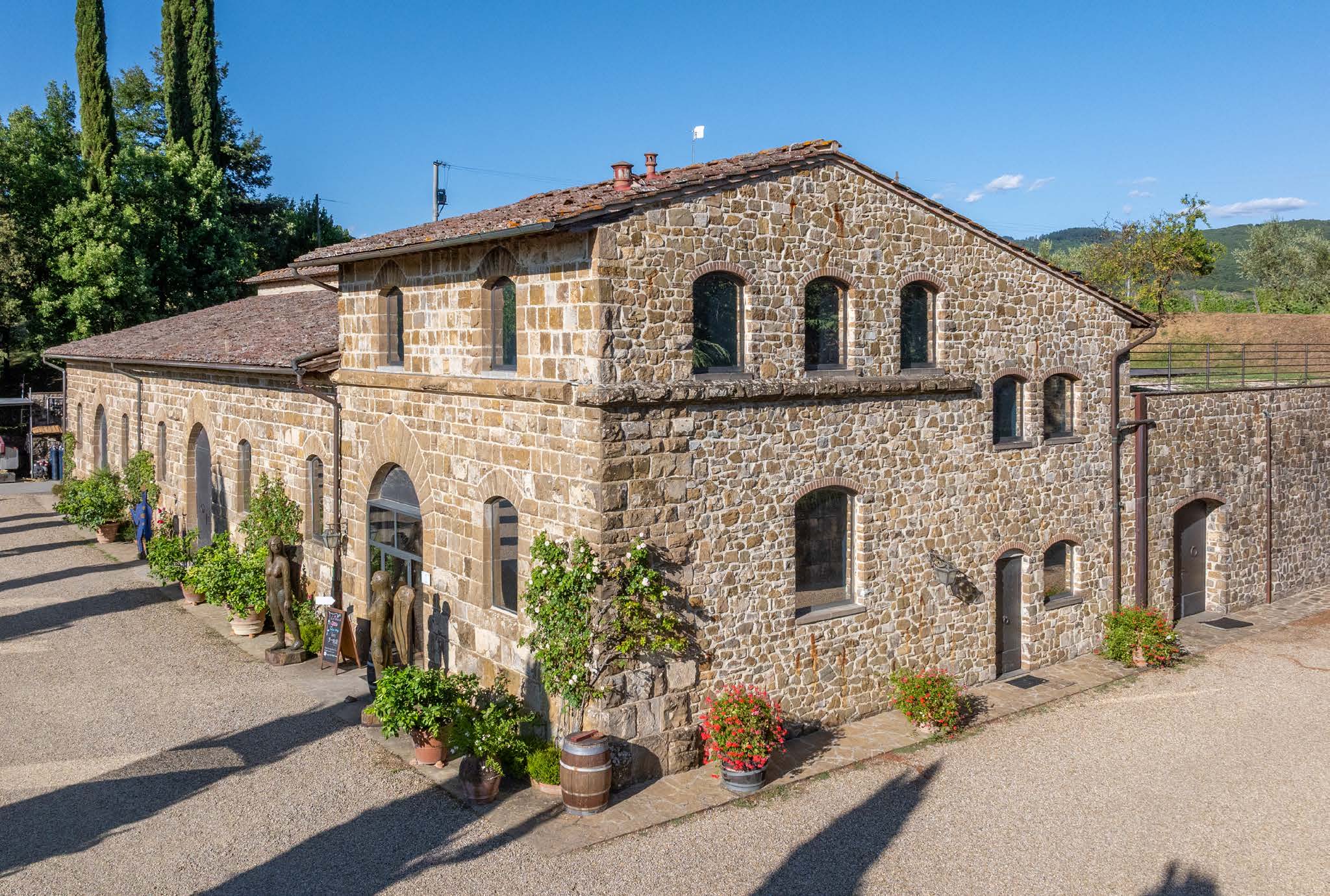 A large stone winery building with tiled roof, surrounded by greenery