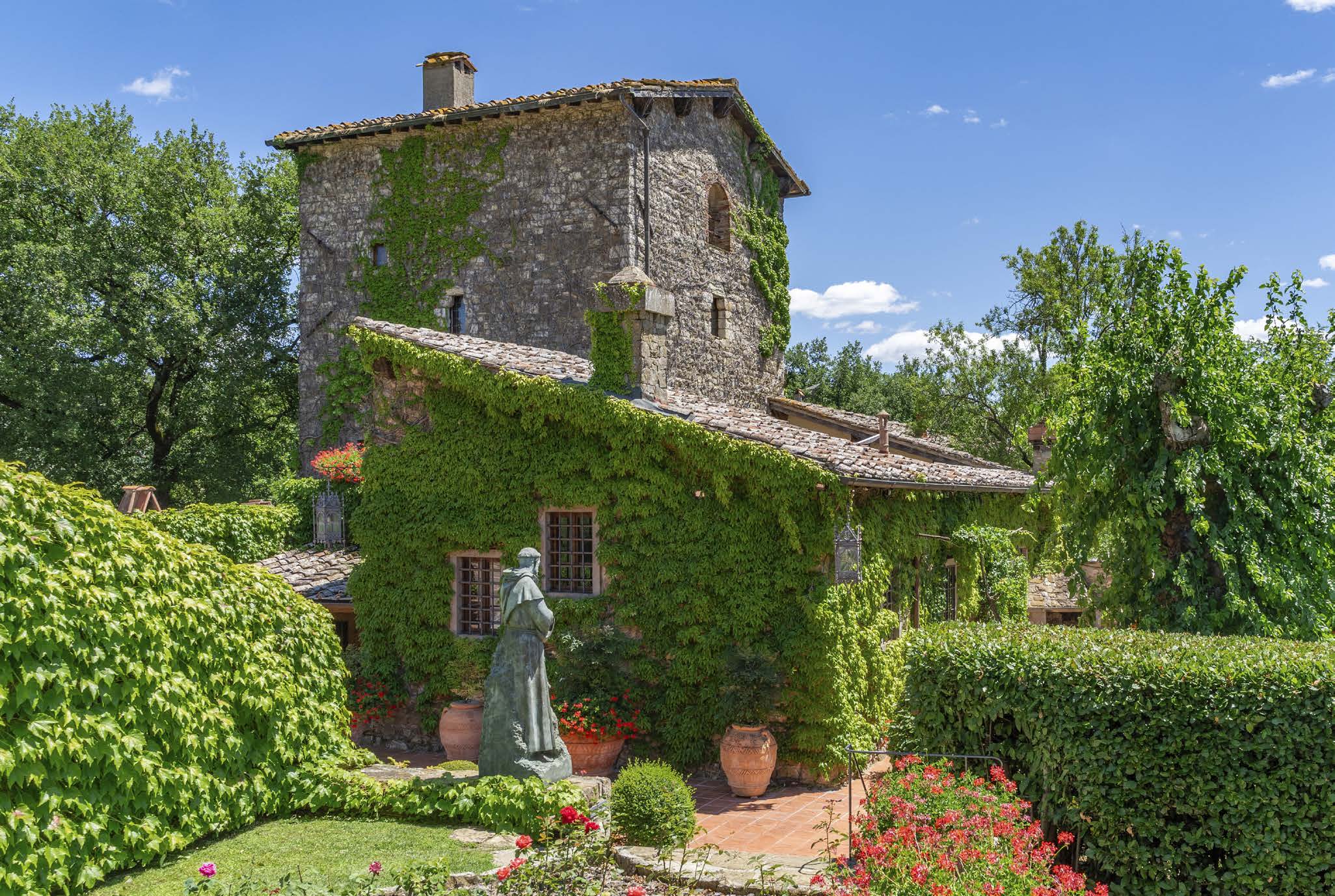 Stone façade of the villa covered in ivy with a garden statue